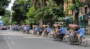 Bicycle rickshaws drivers carrying passengers down the street in Hanoi.